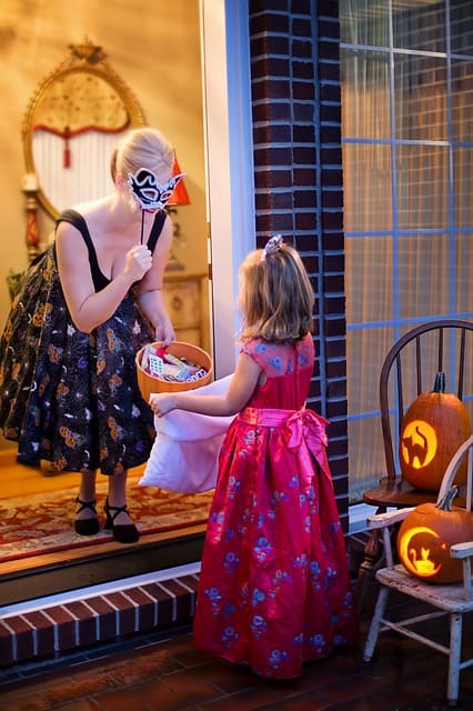 Young trick-or-treater getting candy from masquerade woman